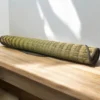 Rolled handmade river grass mat with black edging placed on a wooden surface in natural sunlight
