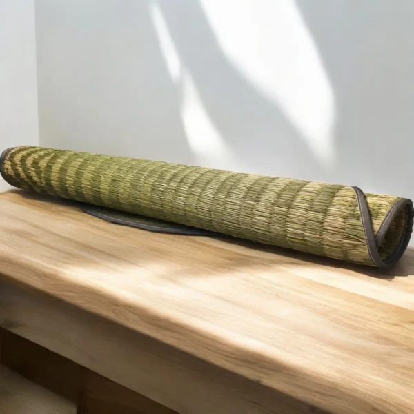 Rolled handmade river grass mat with black edging placed on a wooden surface in natural sunlight