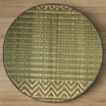 Top view of a handmade 2ft round river grass mat with traditional pattern and black edge on wooden floor