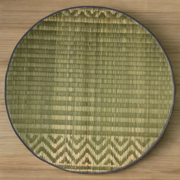 Top view of a handmade 2ft round river grass mat with traditional pattern and black edge on wooden floor