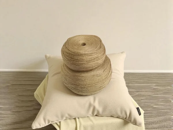 Two large rolls of natural jute twine placed on a cream-colored cushion and folded fabric against a neutral background.