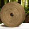 A large roll of natural jute twine placed on a white surface with a lush green forest background.