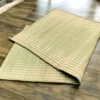 Folded natural handwoven Madurkathi grass mat placed on a wooden floor.
