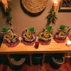Handmade multicolor burnt clay Ganesha musician figurines set of four with green caps and vibrant details, displayed on a wooden table in a warm, cozy indoor setting with candles and wall décor.