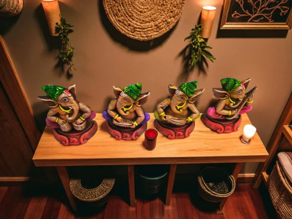 Handmade multicolor burnt clay Ganesha musician figurines set of four with green caps and vibrant details, displayed on a wooden table in a warm, cozy indoor setting with candles and wall décor.