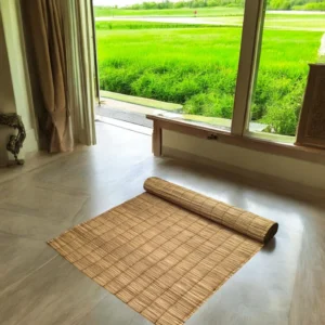 Handmade river grass mat partially rolled on a clean indoor floor with a scenic view of green fields through large windows – eco-friendly and foldable mat, size 3x7 ft.