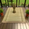 Madurkathi grass mat with ethnic border placed on a wooden veranda floor with a bunch of dried grass and potted plants.