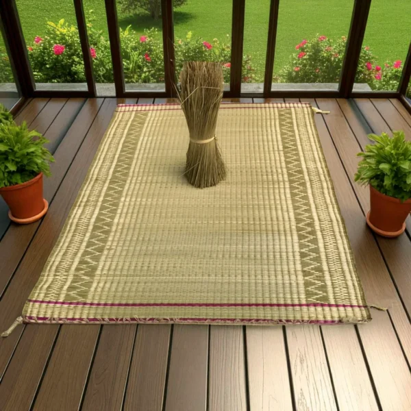 Madurkathi grass mat with ethnic border placed on a wooden veranda floor with a bunch of dried grass and potted plants.
