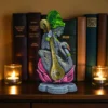 Clay Saraswati idol with veena and swan on a lotus base, placed between lit candles and books on a wooden shelf.