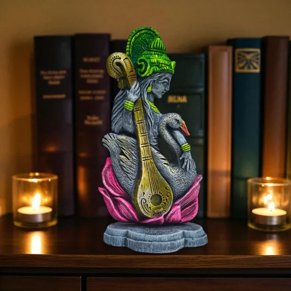 Clay Saraswati idol with veena and swan on a lotus base, placed between lit candles and books on a wooden shelf.