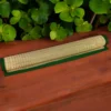 Rolled handwoven river grass mat with green border placed on a wooden surface with green leaves in the background.