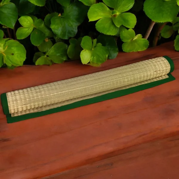 Rolled handwoven river grass mat with green border placed on a wooden surface with green leaves in the background.