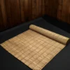 Rolled handmade natural river grass mat on a dark floor with wooden wall background – eco-friendly, foldable, 3x7 feet.