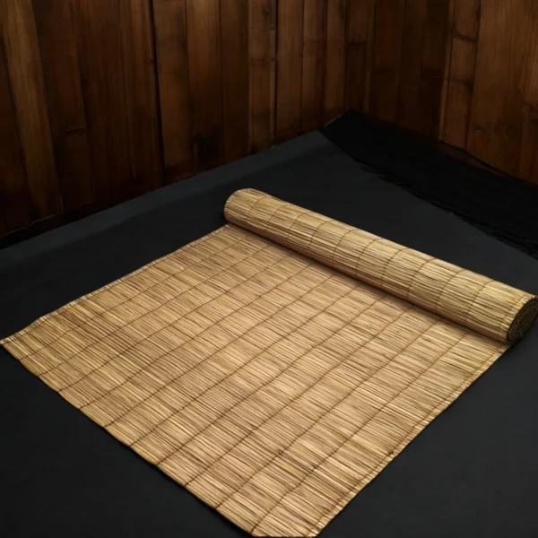 Rolled handmade natural river grass mat on a dark floor with wooden wall background – eco-friendly, foldable, 3x7 feet.