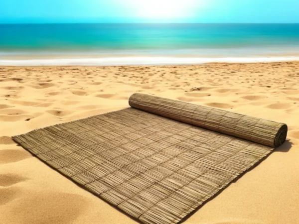Handmade natural river grass mat partially rolled out on golden sand at the beach with a bright blue ocean in the background — eco-friendly, 3x7 ft.
