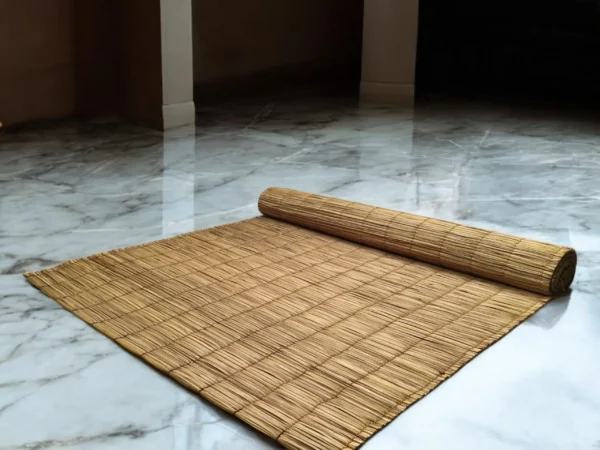 Rolled handmade river grass mat on a glossy marble floor in a minimalist indoor setting — natural, eco-friendly, and 3x7 ft in size.