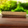 Rolled handmade river grass mat placed on a polished wooden surface with blurred greenery in the background — eco-friendly, natural, 3x7 ft mat.