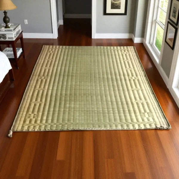 Handwoven Korai grass mat laid on wooden bedroom flooring beside a bed and large window