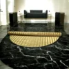 Partially unrolled 4ft round Madurkathi river grass mat on a black marble floor in a modern, elegant room with a black sofa