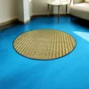 4ft round river grass (Madurkathi) rug on a bright blue floor near a modern sofa and side table in a sunlit room