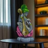 Handcrafted clay Saraswati idol with veena and swan, displayed on a black table in a modern living room with bookshelf and window.