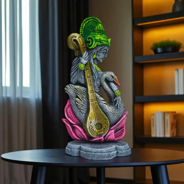 Handcrafted clay Saraswati idol with veena and swan, displayed on a black table in a modern living room with bookshelf and window.