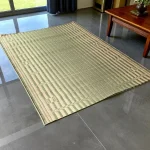 Handwoven double-layer Korai grass mat placed in a modern indoor living room with grey flooring and wooden furniture