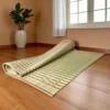 Rolled handwoven Korai grass mat on wooden flooring in a bright room with a plant and window