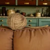 A ball of natural jute twine resting on the backrest of a brown fabric sofa with a kitchen in the background.