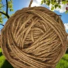 Close-up of a large ball of natural jute twine set outdoors with green grass, trees, and a bright blue sky in the background.