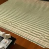 Close-up of a 60x74 inch handwoven Korai grass mat on polished wooden flooring beside a coffee table