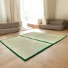 Large handwoven river grass mats with green borders placed in a bright, modern living room with beige floor seating.