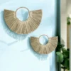 Two handmade half-moon wall hangings crafted from natural grass, displayed on a light blue wall with natural lighting and green plant décor.