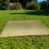 Korai grass mat laid out on a green lawn with blooming flowers and trees in the background