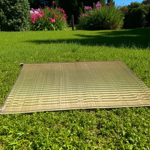 Korai grass mat laid out on a green lawn with blooming flowers and trees in the background