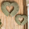 Two handmade heart-shaped wall hangings crafted from natural dried grass, displayed on a bamboo wall panel.