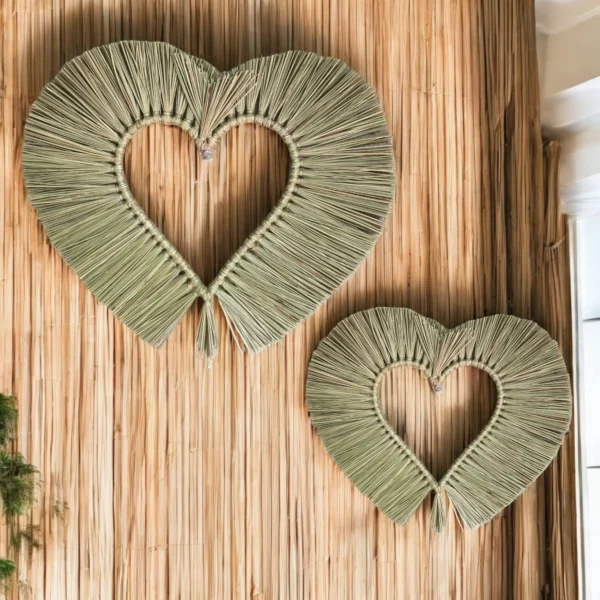 Two handmade heart-shaped wall hangings crafted from natural dried grass, displayed on a bamboo wall panel.