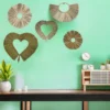 A green wall decorated with five handcrafted natural grass wall hangings in heart, round, and fan shapes, above a minimalist wooden table with plants and decor.