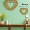 Two circular handmade wall hangings made from natural grass, sized 24 inches and 16 inches, mounted on a neutral beige wall above a wooden table with plants.