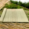 Rolled-out natural Madurkathi grass mat displayed outdoors on bamboo surface with greenery in the background.