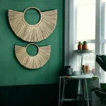Two handmade half-moon wall hangings made of natural grass, displayed on a green wall in a boho-style room with indoor plants and natural light.