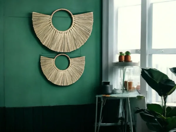 Two handmade half-moon wall hangings made of natural grass, displayed on a green wall in a boho-style room with indoor plants and natural light.