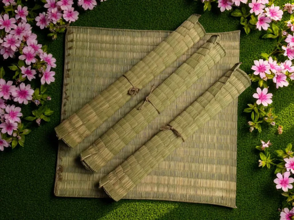 Rolled natural grass mats placed on an open mat, surrounded by pink flowers and green grass.