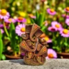 Handmade burnt clay Lord Ganesha statue in brown terracotta finish with painted details, placed outdoors with colorful flowers in the background.
