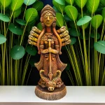 Handmade burnt clay Maa Durga statue placed on a white surface with green leafy plants in the background, showcasing intricate terracotta craftsmanship.