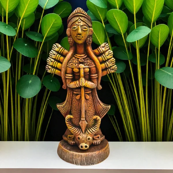 Handmade burnt clay Maa Durga statue placed on a white surface with green leafy plants in the background, showcasing intricate terracotta craftsmanship.