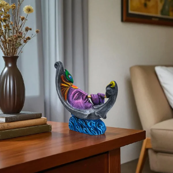 Handmade burnt clay Krishna face decorative statue with peacock feather, placed on a wooden side table beside books and a flower vase in a cozy living room.