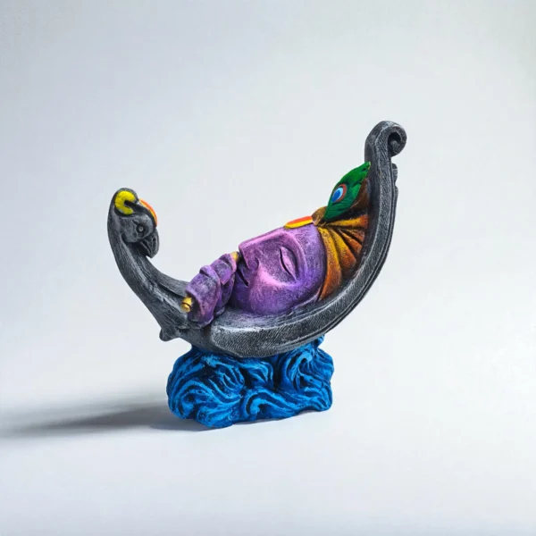 Handmade colorful terracotta Krishna face idol with flute and peacock feather, resting on a decorative wave base.