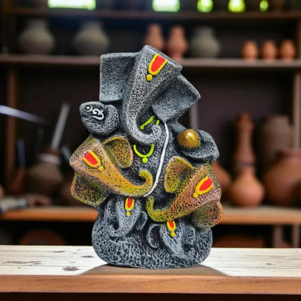 Handmade burnt clay Lord Ganesha statue in black terracotta finish with painted details, placed on a wooden surface in an artisan workshop.