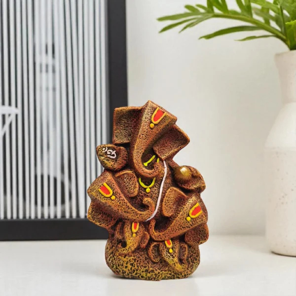 Handmade burnt clay Lord Ganesha statue in brown terracotta finish with painted details, placed on a white tabletop with modern decor.